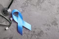 Blue ribbon and stethoscope on grey concrete background, prostate cancer awareness concept. Royalty Free Stock Photo