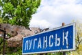 Blue road sign with the inscription in Ukrainian Lugansk, punched by bullets during the war in the Donbass, conflict East Ukraine Royalty Free Stock Photo