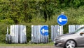 Blue road traffic direction arrow signs on british roundabout on rainy day with cars passing