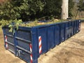 Blue roll off container filled with green waste branches, leaves