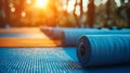 Blue rolled up yoga mat on the wooden floor in the park with blurred background of green trees and warm sunlight in the morning