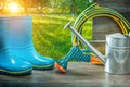 Blue rubber rain boots watering can sprayer gan hose on table in spring sunny sunrise garden