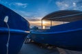 Blue rusting fishing boats on the seashore at sunset. Setting sun reflections in the water against the blue sky and clouds. The Royalty Free Stock Photo