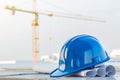 The blue safety helmet and the blueprint at construction site with crane background Royalty Free Stock Photo