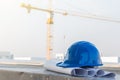The blue safety helmet put on the blueprint at construction site with crane background Royalty Free Stock Photo