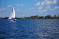 A blue sailboat sails on the lake. The shore and some houses in the background. Yacht sailing in Masuria (Mazury).