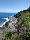 Blue sea of Italy with crashing waves on rocks. Sicily`s seaside made by stone, cliff, plants and trees. Clear blue sky with Royalty Free Stock Photo