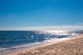 Blue sea sparkling in the sun with a wave, sandy beach and blue sky on a summer day