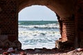 Blue sea waves seascape through red brick arch, view from old brick fort by Baltic Sea