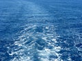 Blue sea waves with white foam. Water behind a ship. Boat wake in the sea, on a brilliant sunny day