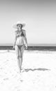 Modern woman in bikini and beach straw hat on seashore walking Royalty Free Stock Photo