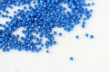 Blue seed beads scattered on a white textile background closeup. Handmade concept Royalty Free Stock Photo