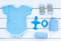 Blue set for newborn boy. Baby bodysuit, socks, airplan toy, oap and powder on white wooden background top view