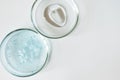 Blue shower gel with scrub grain with bubbles and transparent shampoo smudge in glass petri dish on white background Royalty Free Stock Photo