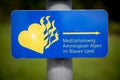 Blue sign in German: Ammergau Alps meditation trail. With a yellow flaming heart