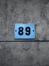 A blue sign with the number 89 (eighty nine). Against a textured stone wall Royalty Free Stock Photo