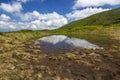 Blue sky with bright white clouds reflected in small lake between green hills on sunny day. Summer panorama Royalty Free Stock Photo