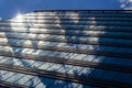 The blue sky with clouds is reflected in the glass of identical windows of modern office building Royalty Free Stock Photo