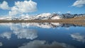 Blue sky with clouds is reflected in the mountain lake. Mountains covered with snow. Royalty Free Stock Photo