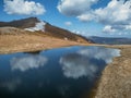 The blue sky with clouds is reflected in the mountainous small reservoir. Mountains covered with snow. Royalty Free Stock Photo