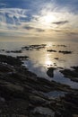 Blue sky at dawn covered by strange cloud formations on a flat sea with black rocks that stand out in the reflection of the sun on Royalty Free Stock Photo