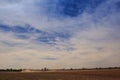 Blue sky fleecy clouds above field tractor in great dust cloud Royalty Free Stock Photo