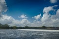 A full river rushes over a weir under wide spring time cumulus clouds in a blue sky Royalty Free Stock Photo