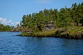 Blue sky over lake. The shore of the island with a green forest and a log cabin of an old house Royalty Free Stock Photo