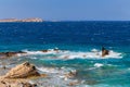 Blue sky over the sea with waves crashing on the rocks in Mykonos, Greece
