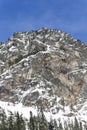 Blue Sky Over Tall Rocky Summit Peak Covered in Winter Snow in Mountain Forest