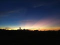 Blue sky with red, yellow and orange tones at sunset and some trees with black tones below in the image