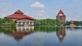 blue sky and some buildings by the lake with a reflection surrounded by trees