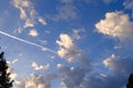 Blue sky, sunny clouds and the white airplane contrail trail, background.