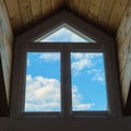 Blue sky and white clouds seen through a large dormer window in a wooden roof