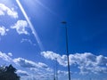 Blue sky with white clouds and sun rays, with silohette lamppost