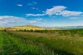 Blue sky with white clouds, trees, fields and meadows with green grass, against the mountains. Composition of nature Royalty Free Stock Photo