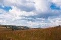 Blue sky with white clouds, trees, fields and meadows with green grass, against the mountains. Composition of nature Royalty Free Stock Photo
