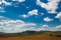 Blue sky with white clouds, trees, fields and meadows with green grass, against the mountains. Composition of nature. Rural summer Royalty Free Stock Photo