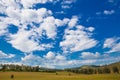 Blue sky with white clouds, trees, fields and meadows with green grass, against the mountains. Composition of nature Royalty Free Stock Photo