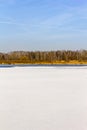 Blue sky, yellow forest in distance, white snowy lake