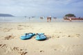 The blue slippers on the beach with white sand, against the background of the sea. Royalty Free Stock Photo