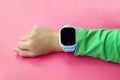 Blue smart digital watch on boy hand with green sleeve on pink background. Modern children technologies. GPS tracker for kids, Royalty Free Stock Photo