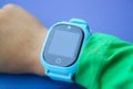 Blue smart digital watch on boy hand with green sleeve. Modern children technologies. GPS tracker for kids, child tracking and Royalty Free Stock Photo