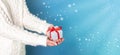 on a blue snowy background, hands hold a box with a gift tied with a red ribbon Royalty Free Stock Photo