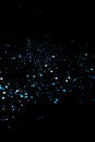 Blue sparkles or glitter over black cosmic abstract background. Royalty Free Stock Photo