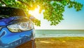 Blue sport SUV car parked by the tropical sea under umbrella tree. Summer vacation at the beach. Summer travel by car. Road trip.