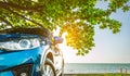 Blue sport SUV car parked by the tropical sea under umbrella tree. Summer vacation at the beach. Summer travel by car. Road trip. Royalty Free Stock Photo