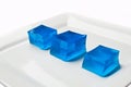 Blue squares of wiggly Jello on a white plate against a white background