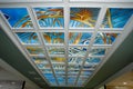 Blue stained glass on the ceiling in a white frame with colorful hand-painted patterns.