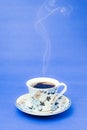 Blue stamped mug with steaming coffee. Soft smoke. Blue background